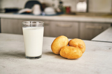 A transparent glass with potato milk on the table next to the potato tubers. 