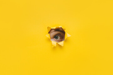 One eye looking through a hole in a yellow paper. Voyeurism. Woman is watching the husband. A curious look. Jealousy, spying on or overhearing the concept. Copy space. - obrazy, fototapety, plakaty