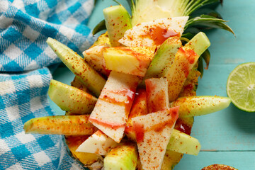 Cucumber, jicama and pineapple with chili powder and chamoy sauce on turquoise background. Mexican snack