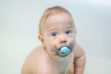 Close-up. Baby with blue eyes with a pacifier with a dirty face on a light, white background