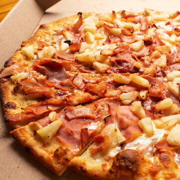 Ham and pineapple pizza called hawaiian on a wooden background