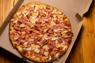 Ham and pineapple pizza called hawaiian on a wooden background