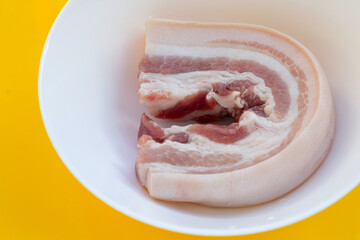 Streaky pork in white bowl on yellow background.