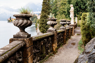 Stone balustrade with vases and statues on the shore. Villa Monastero, Italy