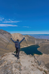 A young man holds his arms open in success after hiking to the top of a nevado de toluca volcano