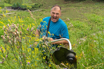 man with a lawn mower. electric trimmer. gardener mows the grass with an electric scythe. grass is...