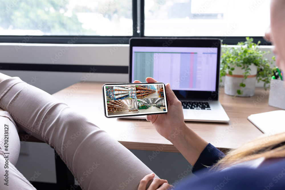 Canvas Prints Caucasian woman holding smartphone with view of warehouse security cameras on screen