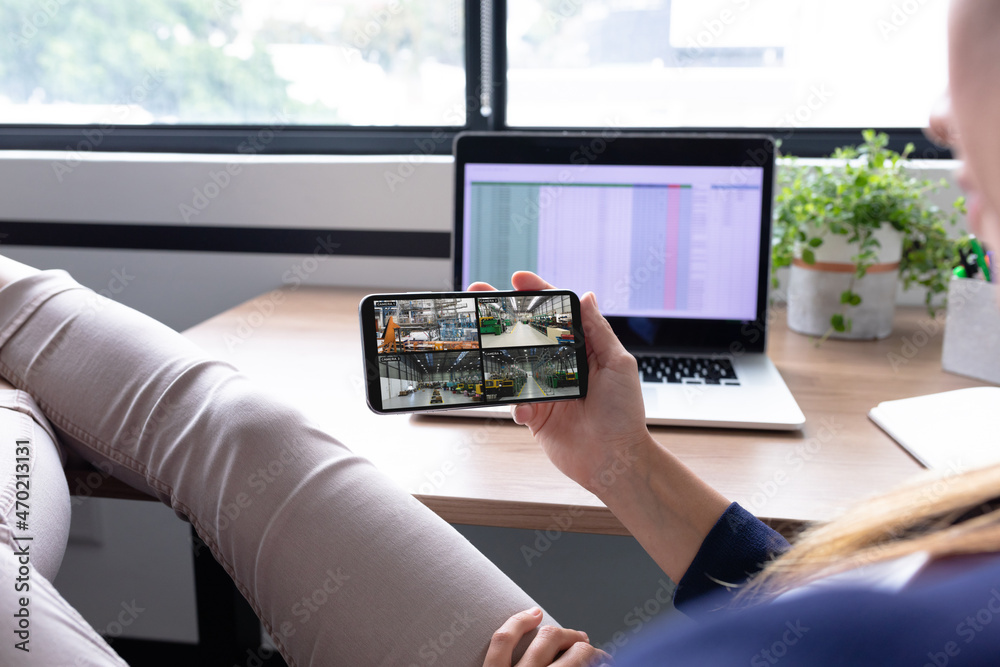 Canvas Prints Caucasian woman holding smartphone with view of warehouse security cameras on screen