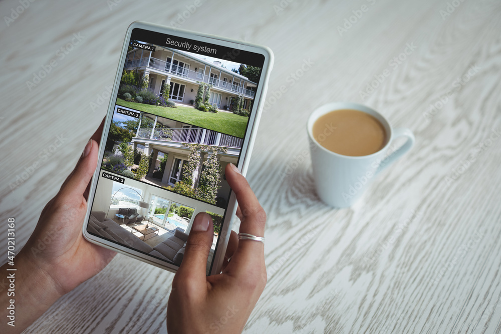 Wall mural Hands of caucasian woman holding tablet with view of home from security cameras on screen