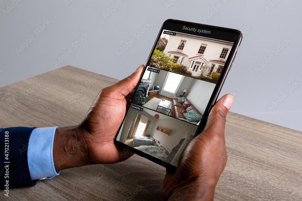 Wall mural Hands of african american man holding tablet with view of home from security cameras on screen