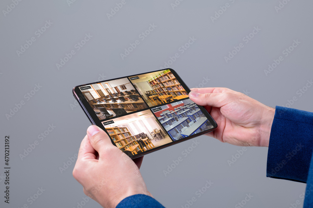 Wall mural Hands of caucasian man holding tablet with view of library from security cameras on screen