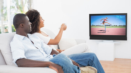Side view of african american couple sitting at home together watching athletics event on tv