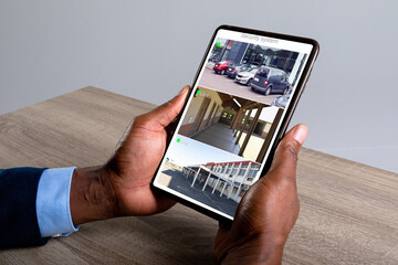 Hands of caucasian man holding smartphone with view from security cameras at workplace on screen