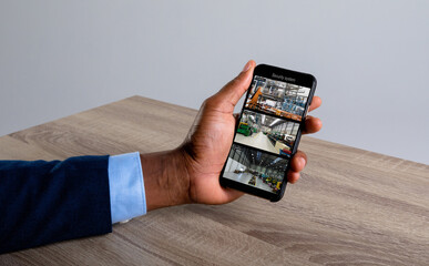 Hand of caucasian man holding smartphone with view of warehouse from security cameras on screen