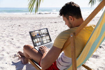 Caucasian man on holiday using laptop with view of gym from security cameras on screen