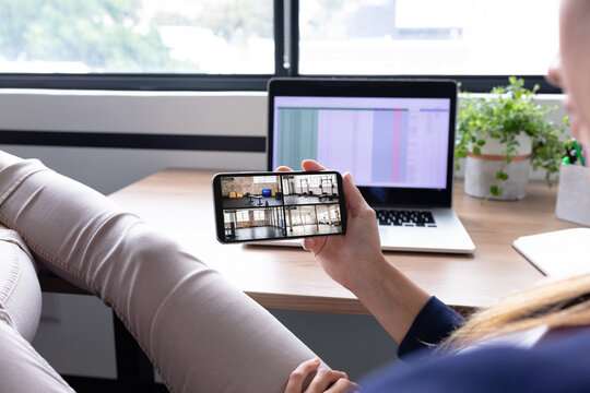 Caucasian woman in office using smartphone with view of gym from security cameras on screen
