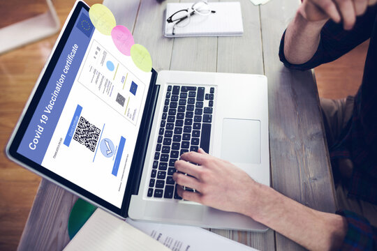 Caucasian man at desk using laptop with covid vaccination certificate and qr code on screen