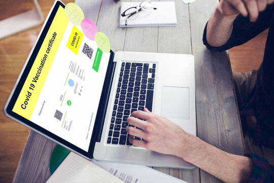Caucasian man at desk using laptop with covid vaccination certificate and qr code on screen