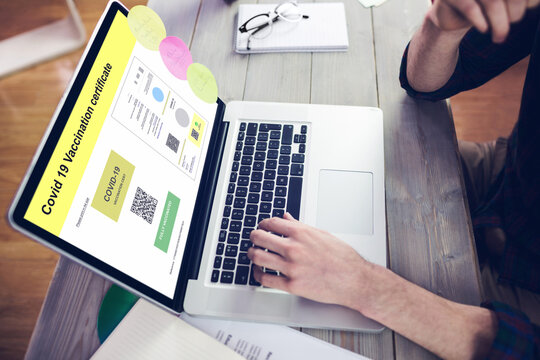 Caucasian man at desk using laptop with covid vaccination certificate and qr code on screen