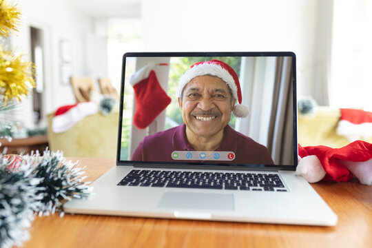 Smiling senior biracial man in santa hat on laptop video call interface screen at christmas