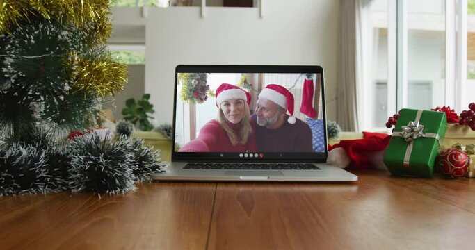 Smiling caucasian couple wearing santa hats on christmas video call on laptop