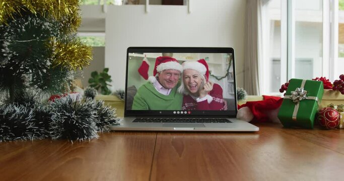 Smiling senior caucasian couple wearing santa hats on christmas video call on laptop