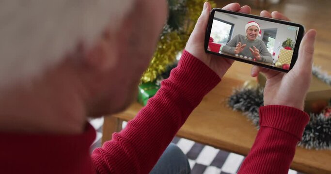 Caucasian man with santa hat using smartphone for christmas video call with smiling man on screen