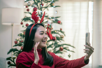 Attractive Asian Woman Video Call Conversation via Smartphone Greeting Christmas, New Year, Christmas Tree Background.