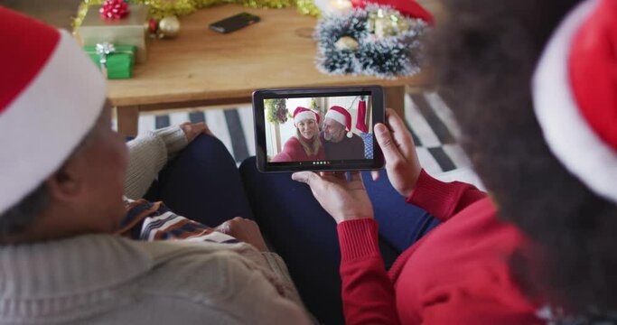 African american mother and daughter using tablet for christmas video call with couple on screen