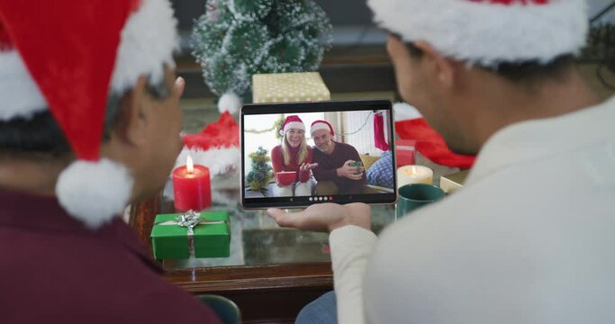 Biracial father and son with santa hats using tablet for christmas video call with couple on screen