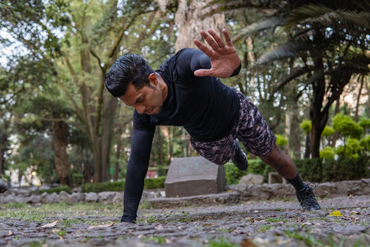 Entrenador latino concentrado realizando rutina de plancha con extensión cruzada en parque deportivo