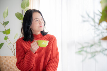 コーヒーを飲みながらくつろぐアジア人（日本人）女性　コピースペースあり