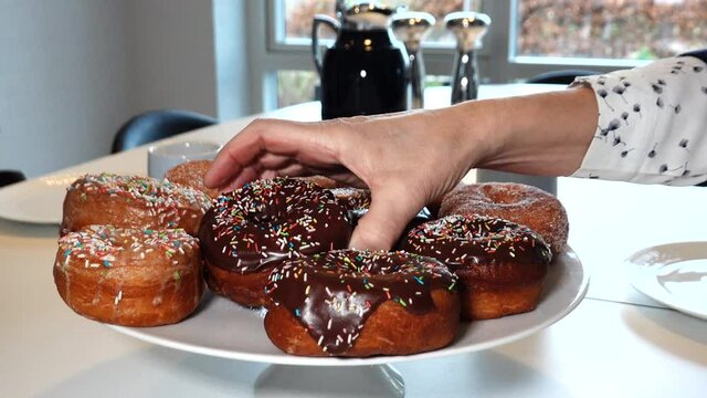A hand grabs a fresh homemade donut from a plate. 