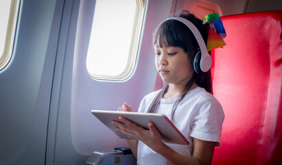 Young tourist girl passenger flight seat near window using smartphone app relax litsening music bluetooth headphones noise-cancelling using wifi internet connection on board