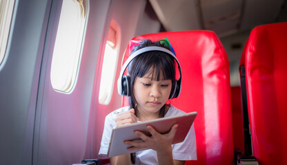Young tourist girl passenger flight seat near window using smartphone app relax litsening music bluetooth headphones noise-cancelling using wifi internet connection on board