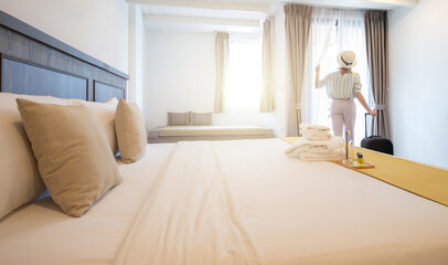 Rear view of young tourist woman looking to view outside window in hotel bedroom after check-in. Conceptual of travel and vacation lifestyle.