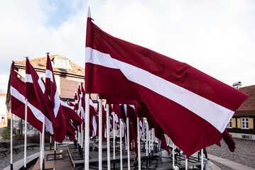 Lots of Latvian red and white flags on the day of proclamation of the Republic of Latvia. - obrazy, fototapety, plakaty