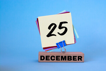 December 25th. Day 25 of December month, calendar on workplace with blue background. Winter time.