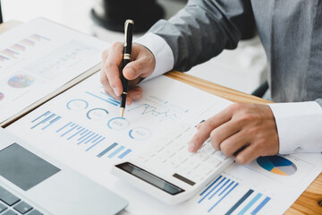 Businessman working with finance calculate on calculator and using computer laptop and document data chart in office room.