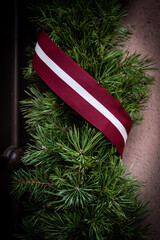 Home decoration with pine branches and ribbon in the color of the Latvian flag. Day of proclamation of the Republic of Latvia - obrazy, fototapety, plakaty