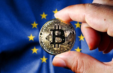 Hold the physical version of Bitcoin (the new virtual currency) and the European Union flag. EU...