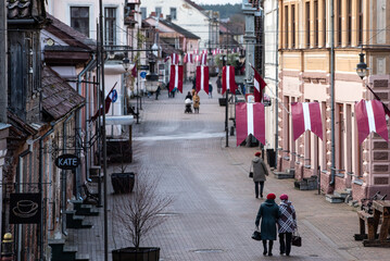 Pedestrian street with people and Latvian red and white flags. Day of proclamation of the Republic of Latvia. Kuldiga, Latvia. Aerial view