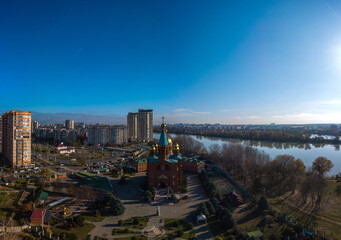 The western outskirts of the YMR microdistrict in the city of Krasnodar near the Kuban River. Multi-storey buildings, a small classical Orthodox church with golden domes, a tramway circle  - obrazy, fototapety, plakaty