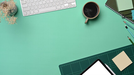 Top view wireless keyboard, coffee cup, digital tablet and stationery on green background.