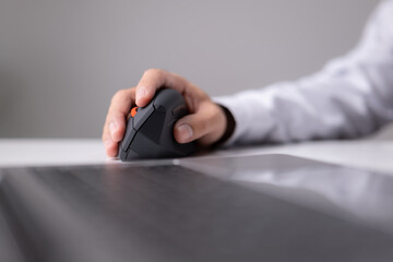 A modern laptop and a vertical mouse in a panoramic shot. An ergonomic vertical mouse is used by a...
