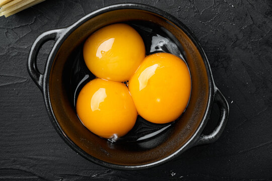 Bright yellow egg yolks, on black stone background, top view flat lay