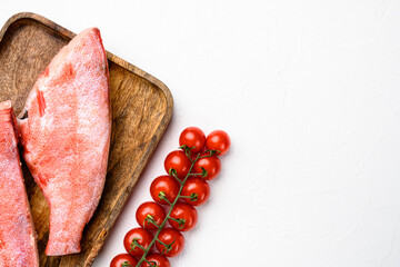 Raw red sea bass fish, on wooden serving board, on white stone table background, top view flat lay, with copy space for text