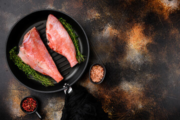 Fish raw snapper, in frying cast iron pan, on old dark rustic table background, top view flat lay, with copy space for text