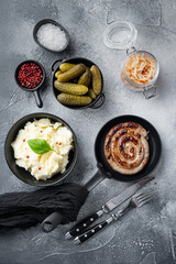 Fototapeta na wymiar Traditional German Sausages with Mashed Potatoes and Sauerkraut in cast iron frying pan, on gray background, top view flat lay