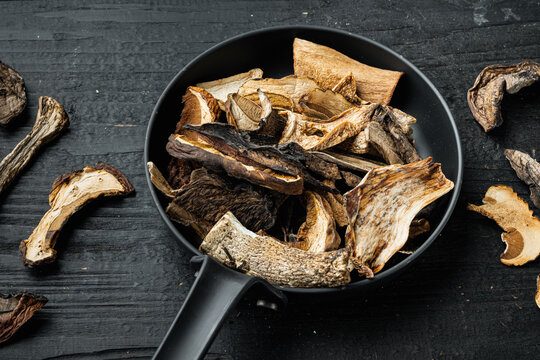 Dried wild mushrooms in cast iron frying pan, on black wooden table background